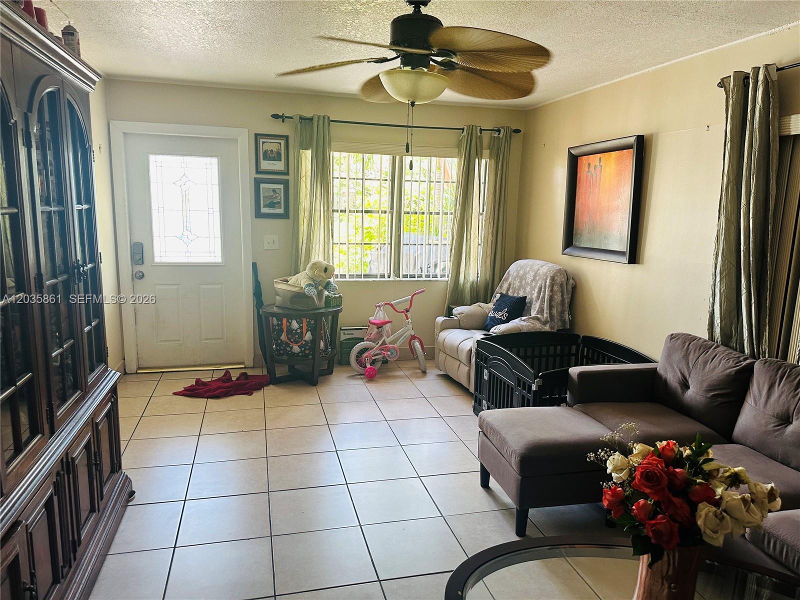 A living room features tile flooring, a ceiling fan, a front door, and furniture — MIAMI, FL