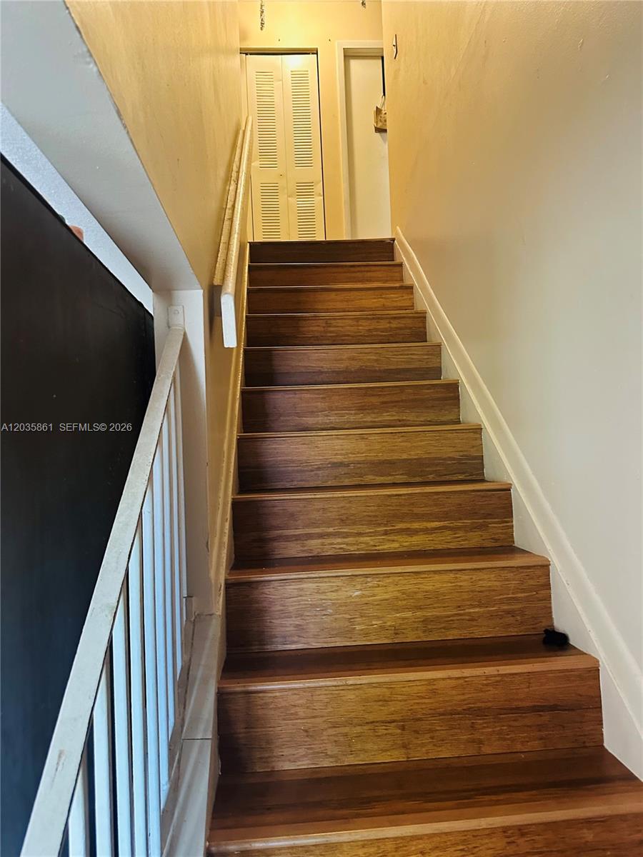 A wooden staircase with a white railing leads upward toward a closed closet door — MIAMI, FL