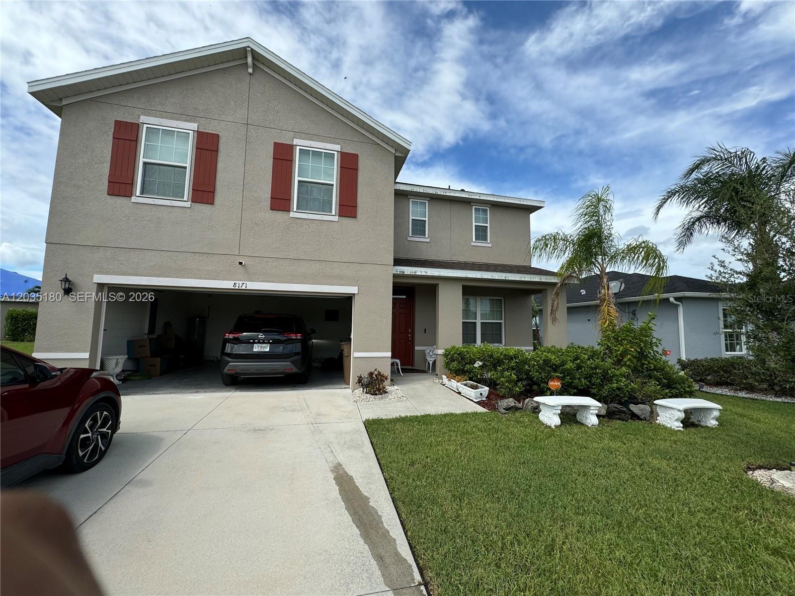 A two-story suburban house features a tan stucco exterior, red shutters, and a two-car garage — 8171 Gopher Tortoise Trl, Lehigh Acres FL 33972, LEHIGH ACRES, FL