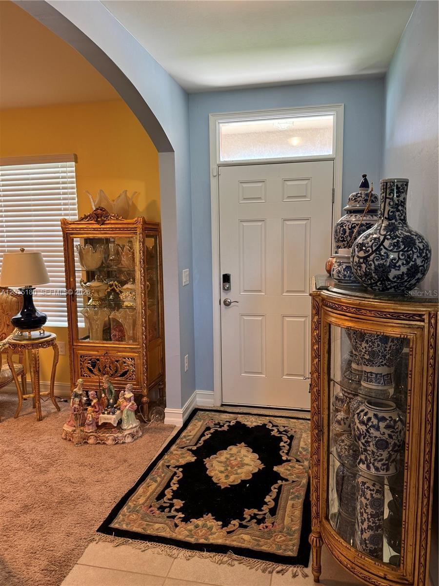 An entryway features a white door, two ornate gold display cabinets, and a patterned rug — 8171 Gopher Tortoise Trl, Lehigh Acres FL 33972, LEHIGH ACRES, FL