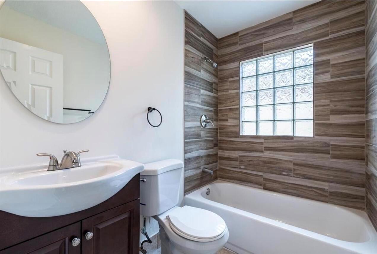 A bathroom features a wood-look tiled shower surround, a glass block window, and a vanity — 4147 Meade Way, West Palm Beach FL 33409, WEST PALM BEACH, FL