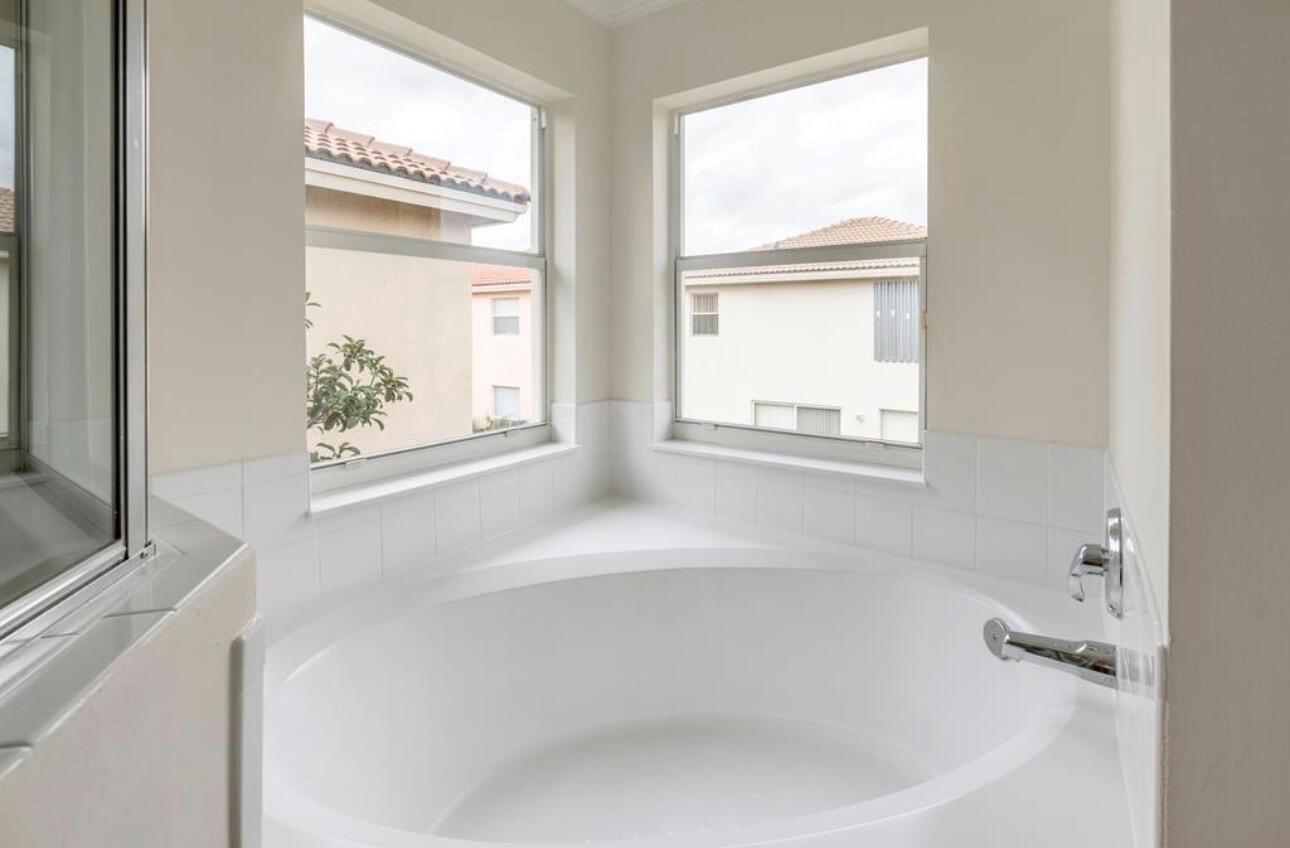 A white soaking tub sits in a corner beneath two windows in a bathroom — 4147 Meade Way, West Palm Beach FL 33409, WEST PALM BEACH, FL
