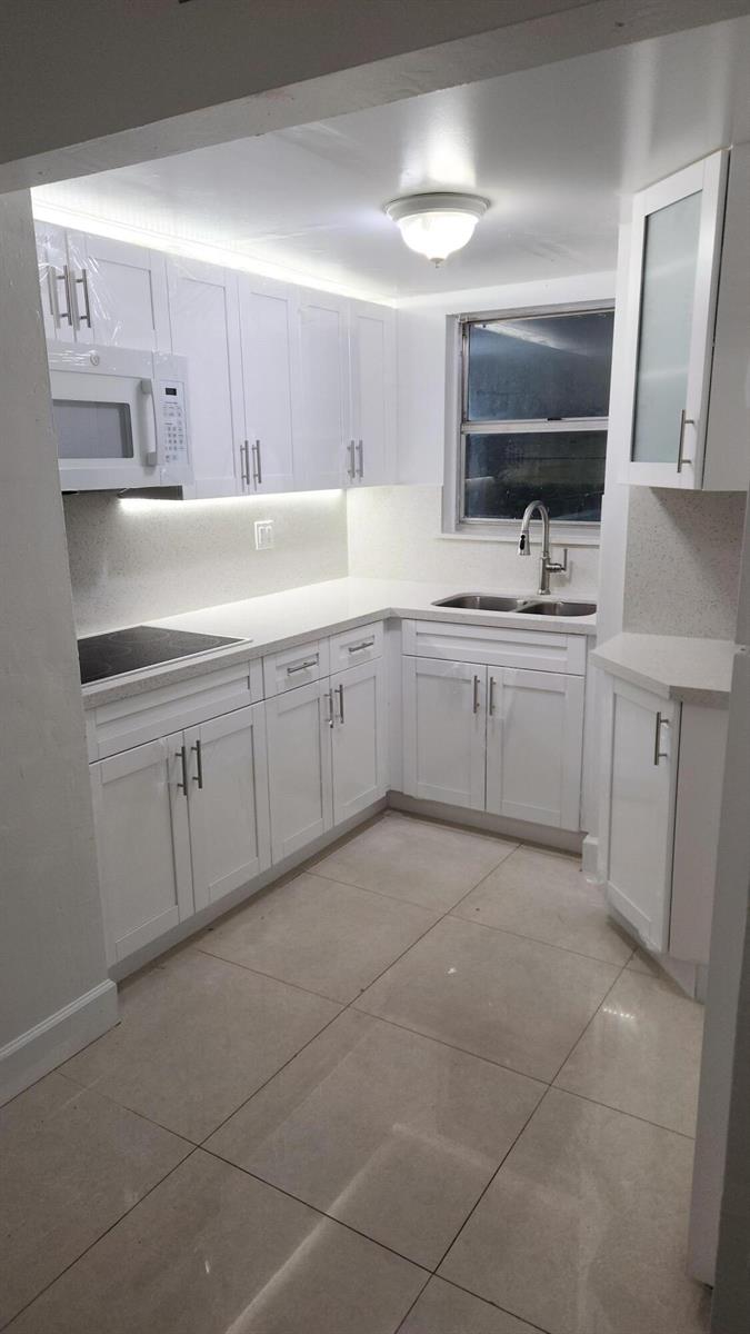 A white kitchen features shaker-style cabinets, quartz countertops, a stainless steel sink, and tile flooring — 210 Fontainebleau Boulevard # 311, Miami FL 33172, MIAMI, FL