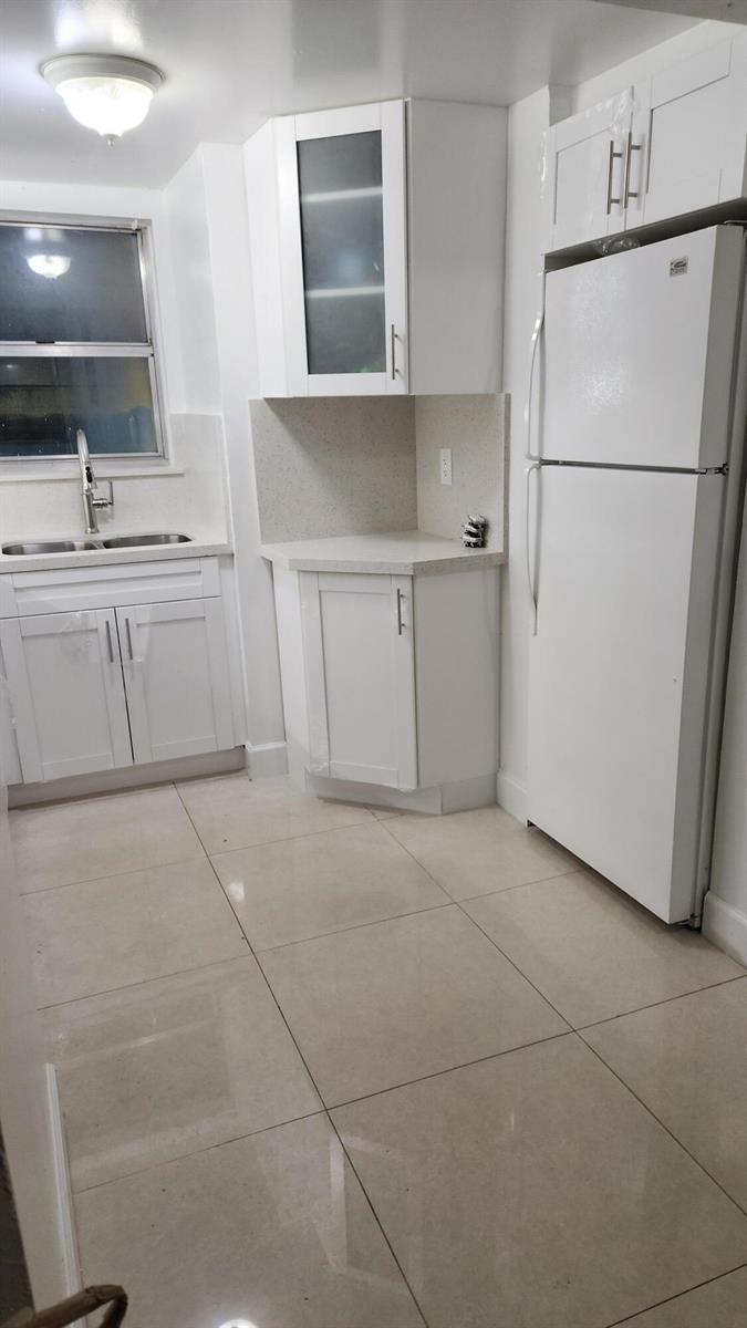 A kitchen features white cabinets, a white refrigerator, a double sink, and light-colored tile flooring — 210 Fontainebleau Boulevard # 311, Miami FL 33172, MIAMI, FL