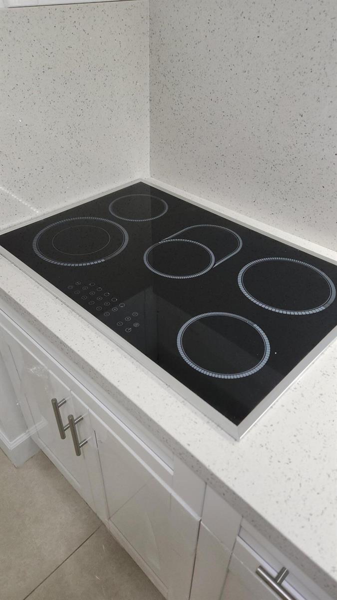 A black electric cooktop is set into a white speckled countertop in a kitchen — 210 Fontainebleau Boulevard # 311, Miami FL 33172, MIAMI, FL