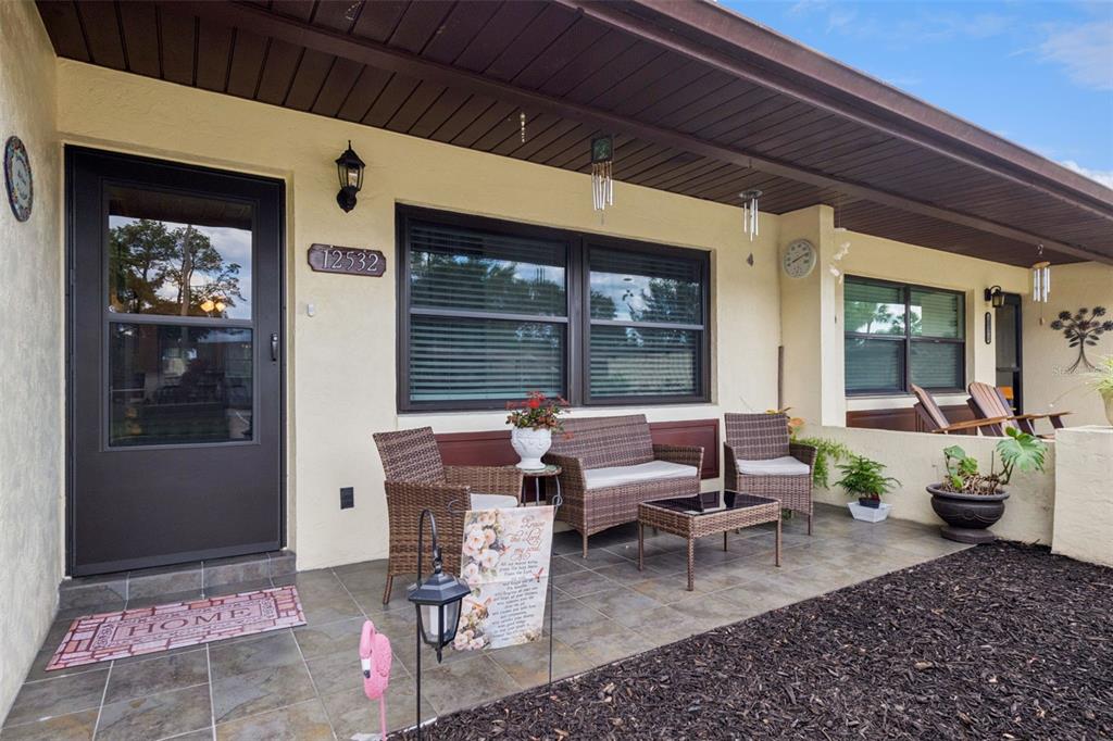 A covered patio features wicker furniture, tile flooring, and a dark-framed front door — 12532 ORANGEWOOD COURT UNIT 0, TAVARES, FL