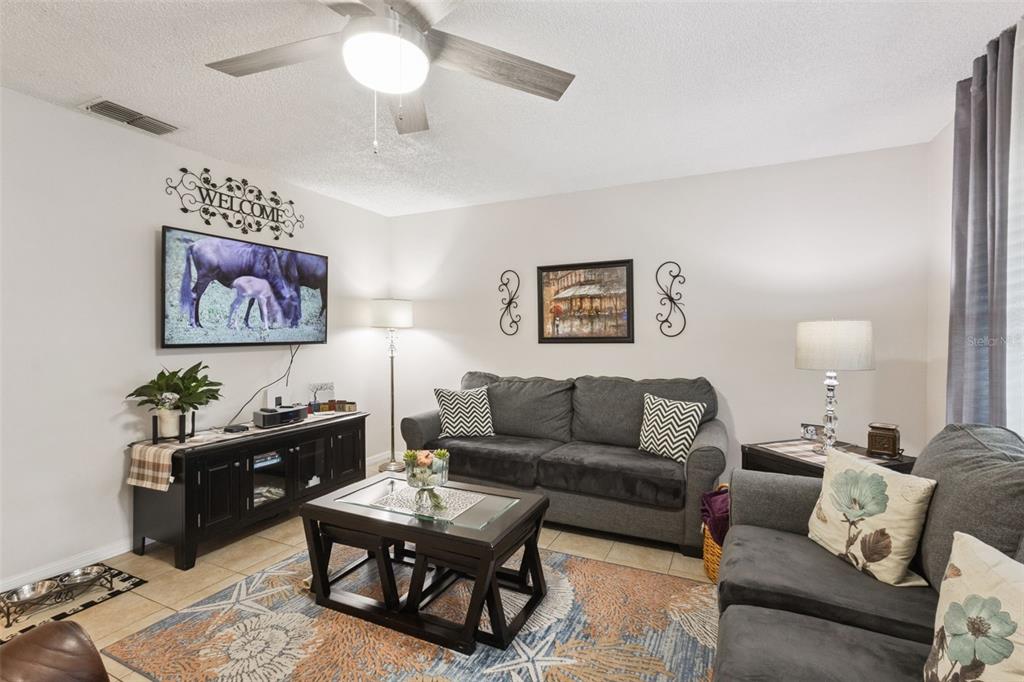 A living room features gray sofas, a dark wood coffee table, and a wall-mounted television — 12532 ORANGEWOOD COURT UNIT 0, TAVARES, FL