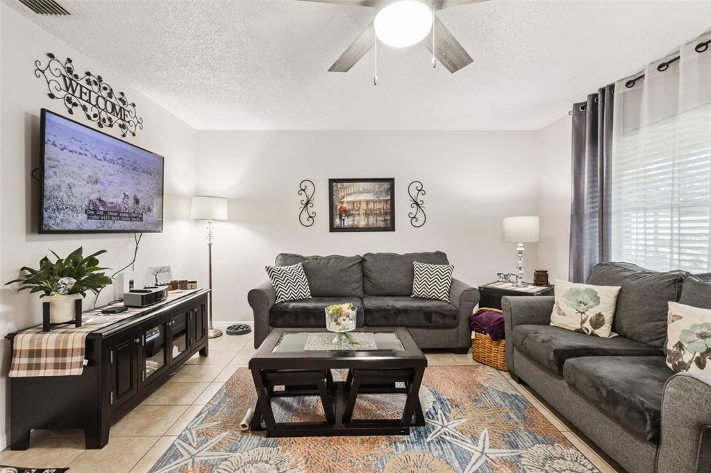 A living room features two dark gray sofas, a coffee table, and a wall-mounted television — 12532 ORANGEWOOD COURT UNIT 0, TAVARES, FL