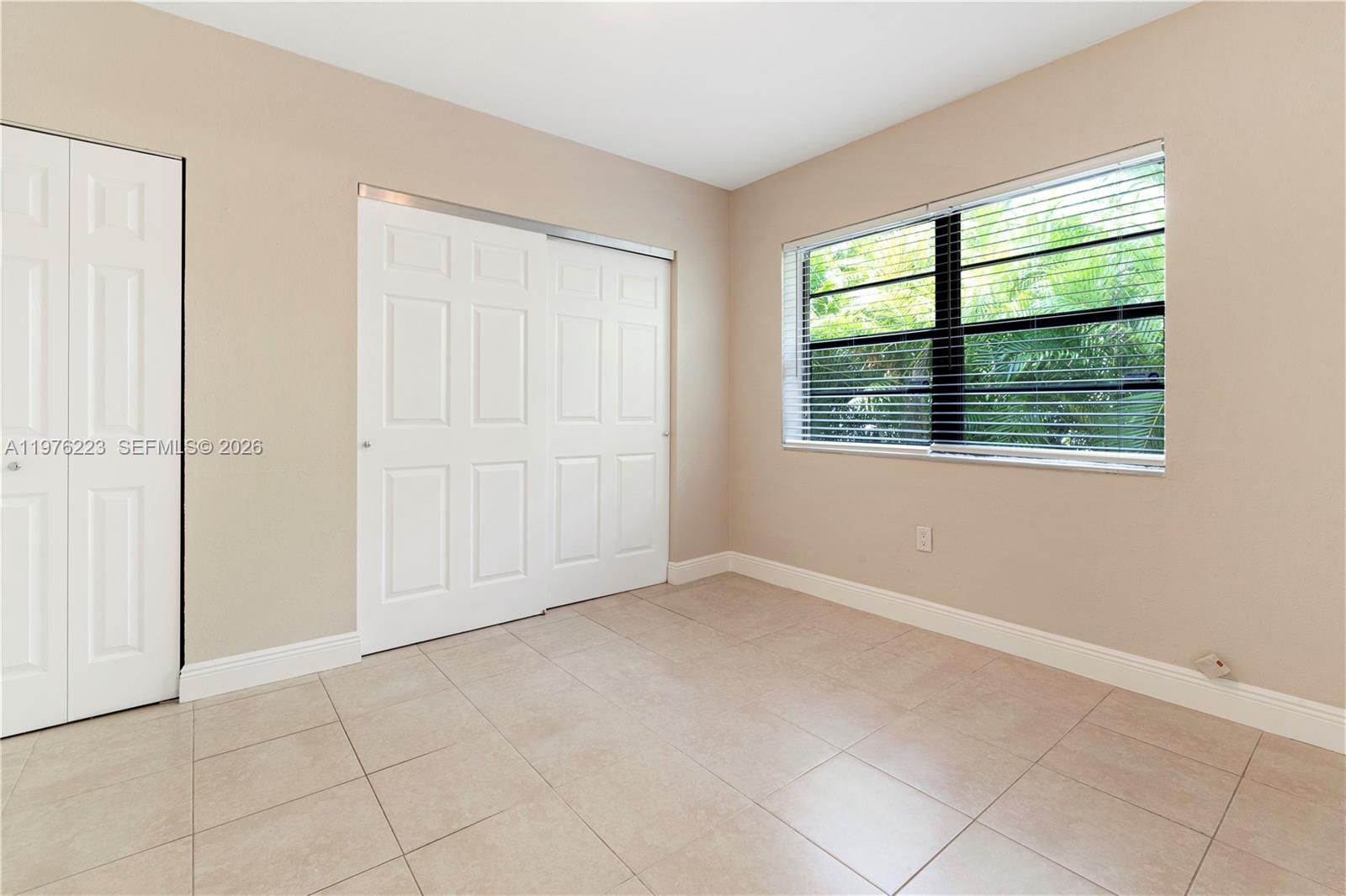 An empty room features beige walls, light tile flooring, white closet doors, and a window — 214 Salamanca Ave # 3, Coral Gables FL 33134, CORAL GABLES, FL