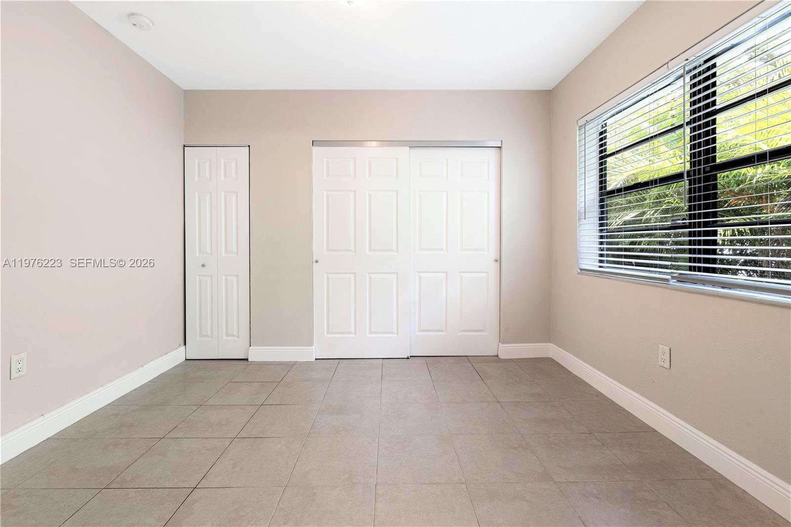 A bedroom features beige walls, gray tile flooring, a window with blinds, and two closets — 214 Salamanca Ave # 3, Coral Gables FL 33134, CORAL GABLES, FL