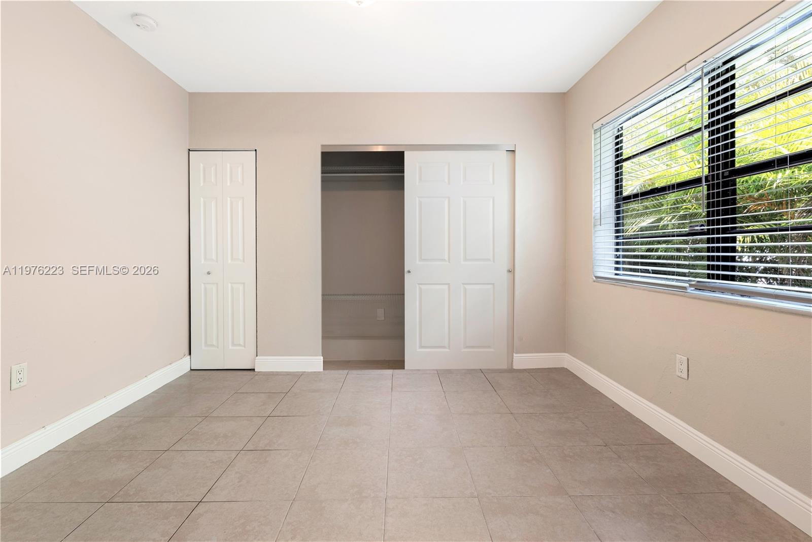 A bedroom with beige walls, tile flooring, a closet, and a window with blinds — 214 Salamanca Ave # 3, Coral Gables FL 33134, CORAL GABLES, FL