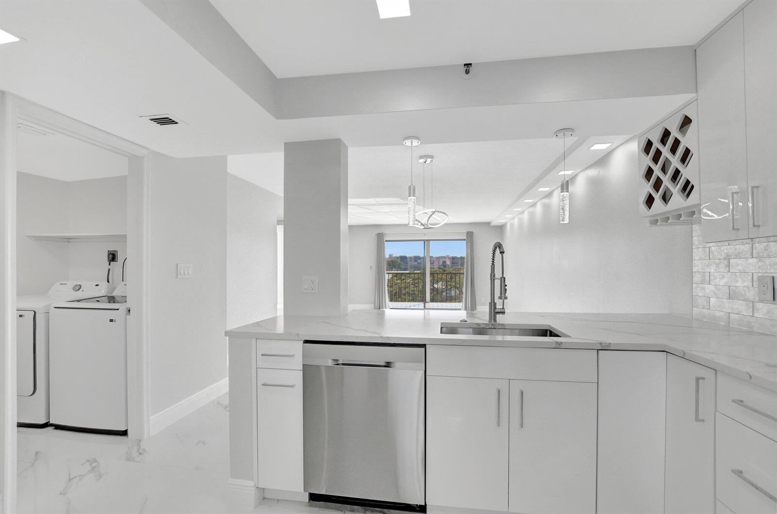 A modern white kitchen with stainless steel appliances, marble countertops, and an adjacent laundry room — 7076 Huntington Lane # 407, Delray Beach FL 33446, DELRAY BEACH, FL