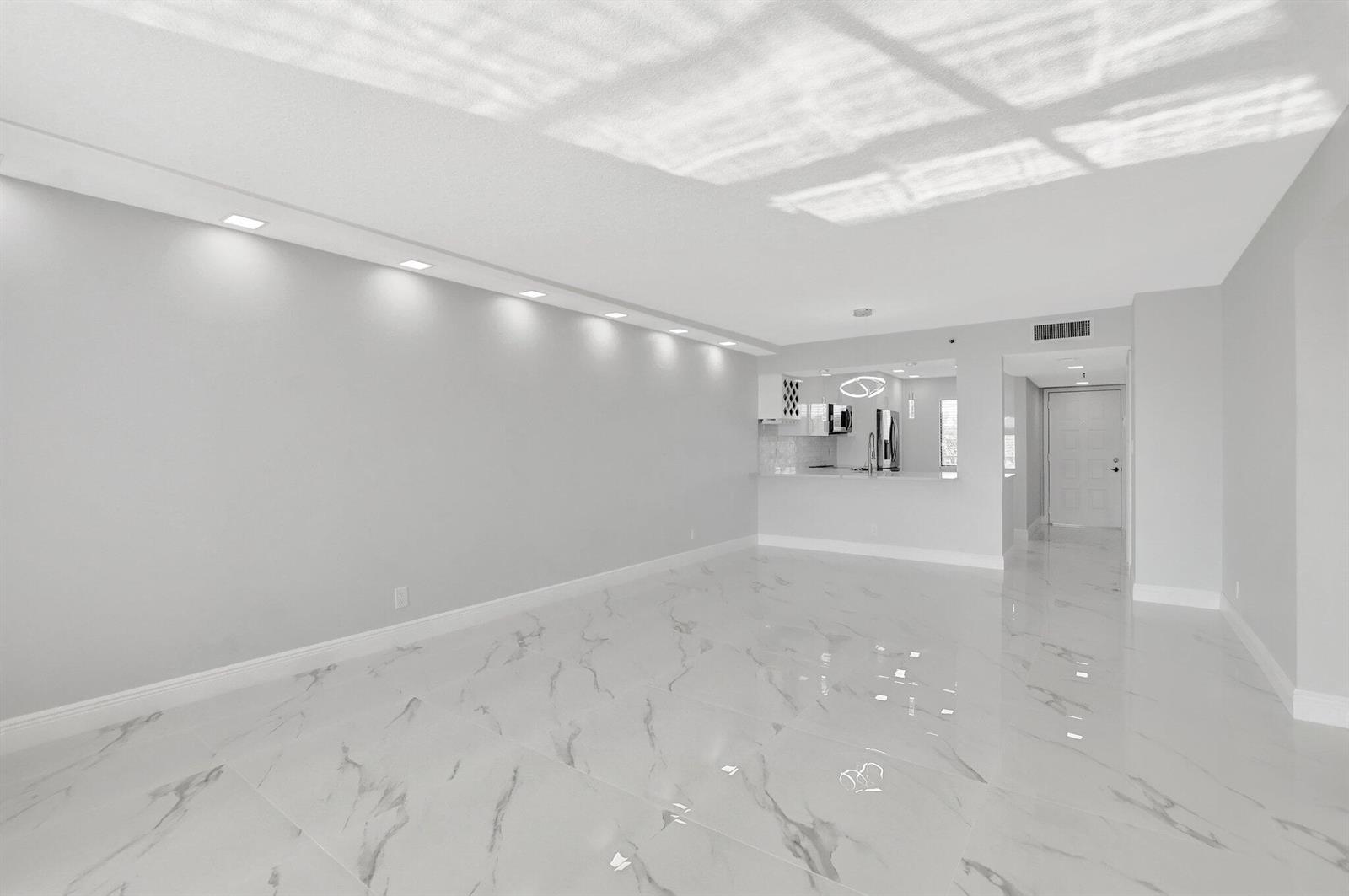 An empty living room with white marble floors, recessed lighting, and an open kitchen area — 7076 Huntington Lane # 407, Delray Beach FL 33446, DELRAY BEACH, FL