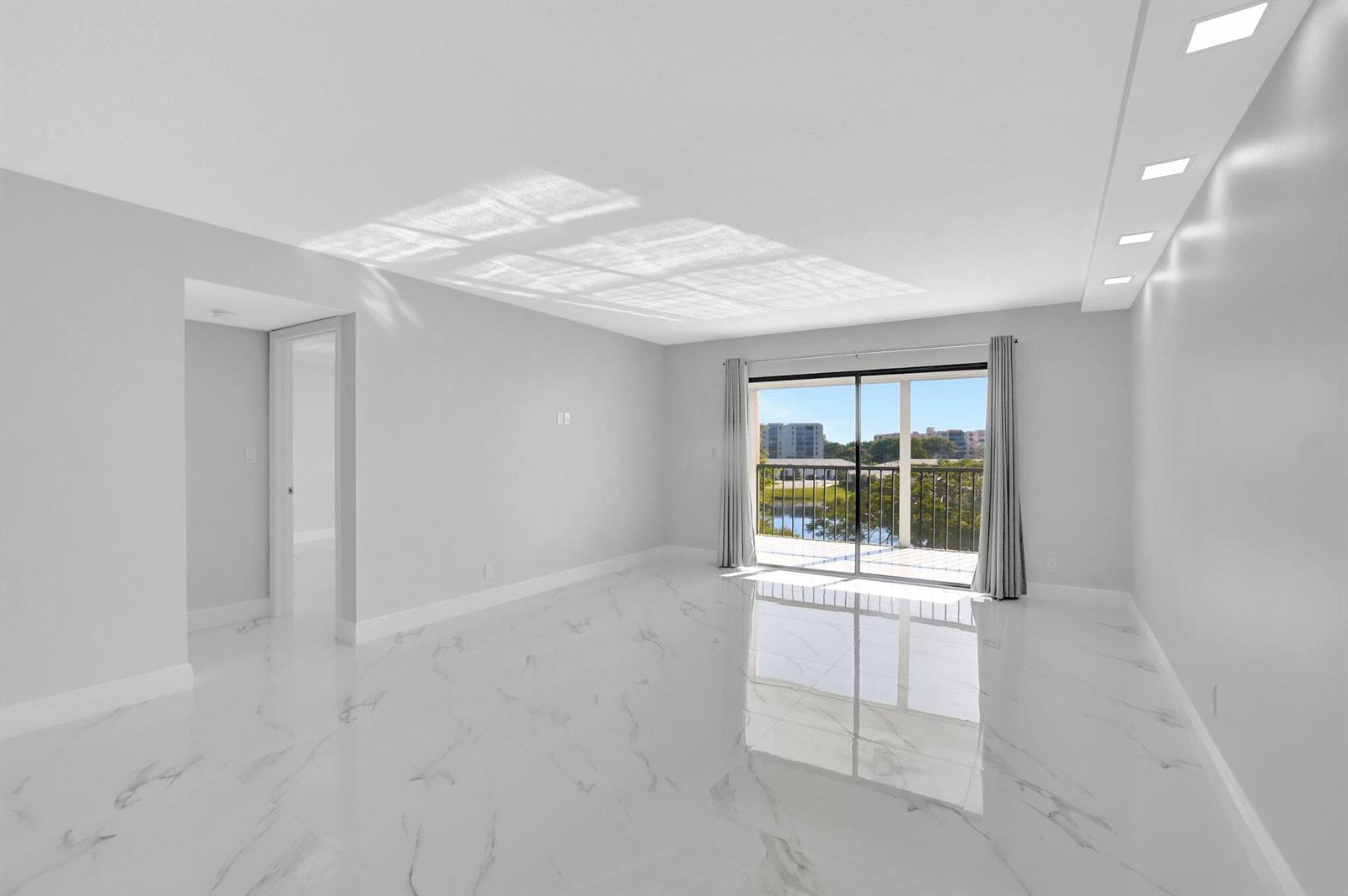 An empty room with white marble floors, recessed lighting, and a sliding glass door to a balcony — 7076 Huntington Lane # 407, Delray Beach FL 33446, DELRAY BEACH, FL