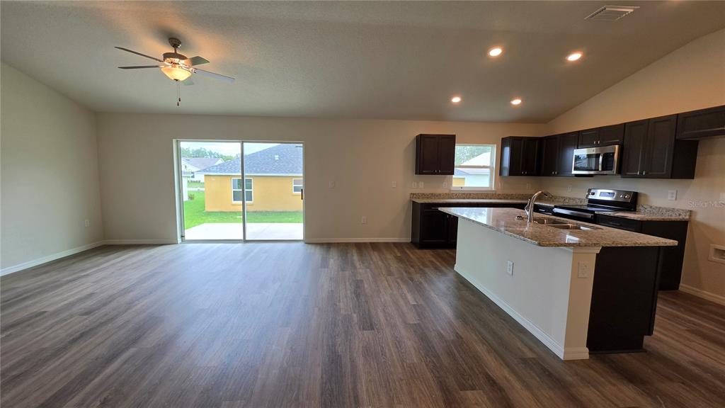 An open-concept kitchen and living area features dark cabinetry, granite countertops, and wood-look flooring — 668 W WALKERTOWN DRIVE, CITRUS SPRINGS, FL