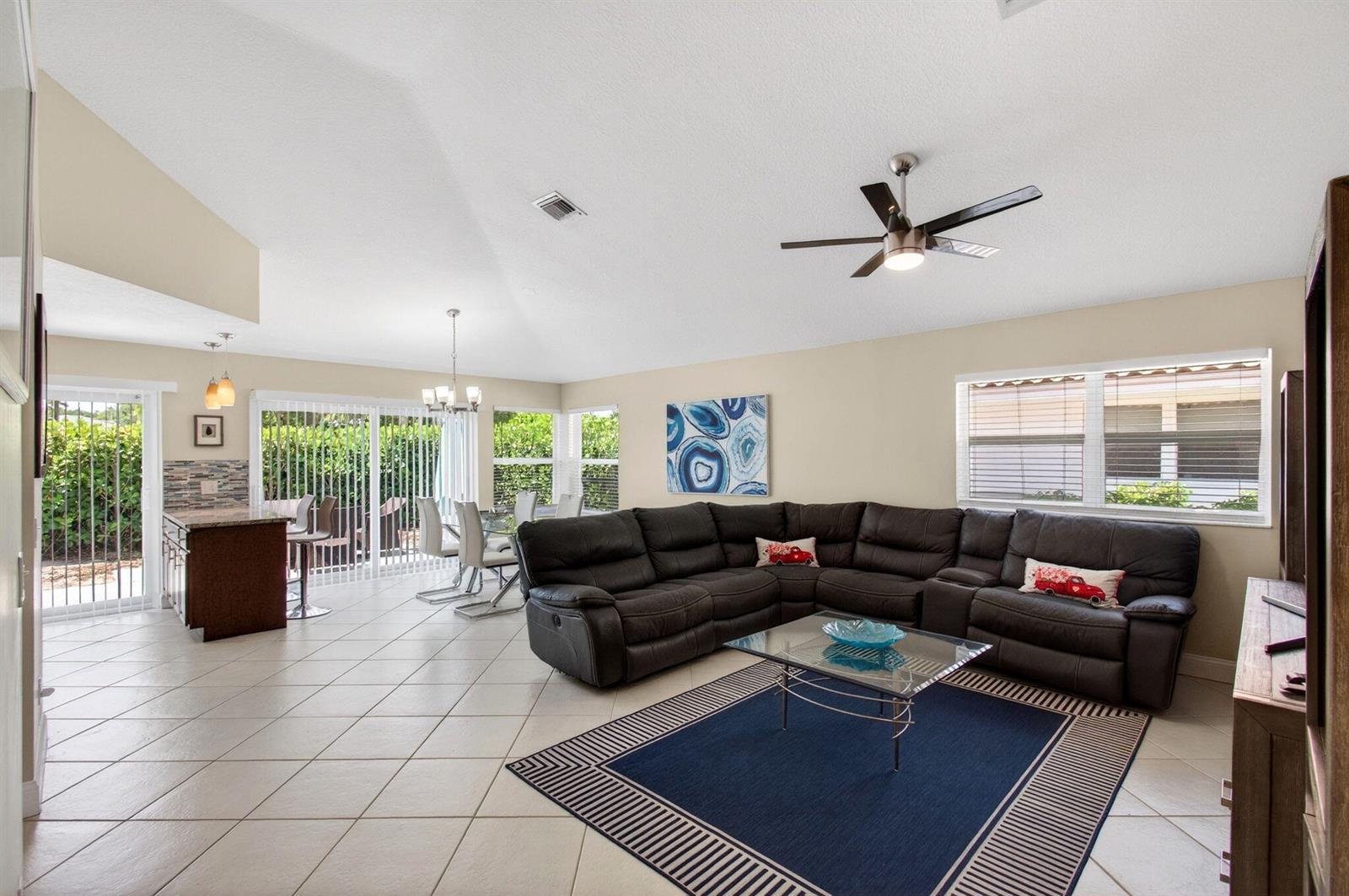 A living room with a large dark sectional sofa, tile floors, and an adjacent dining area — 2034 NW 52nd Street, Boca Raton FL 33496, BOCA RATON, FL