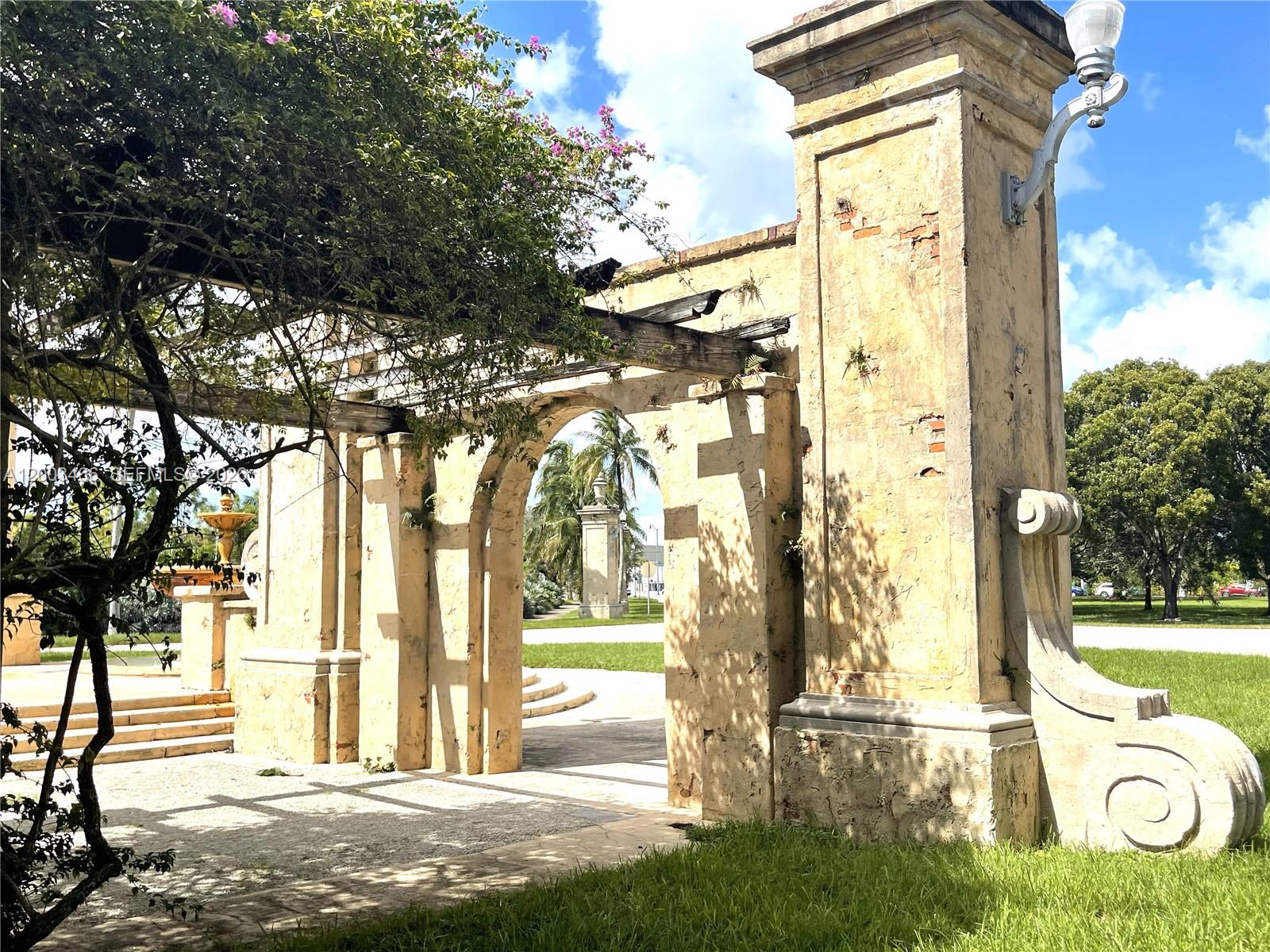A weathered stone archway with a wooden pergola stands in a grassy park setting — 1556 San Benito Ave # 1556, Coral Gables FL 33134, CORAL GABLES, FL