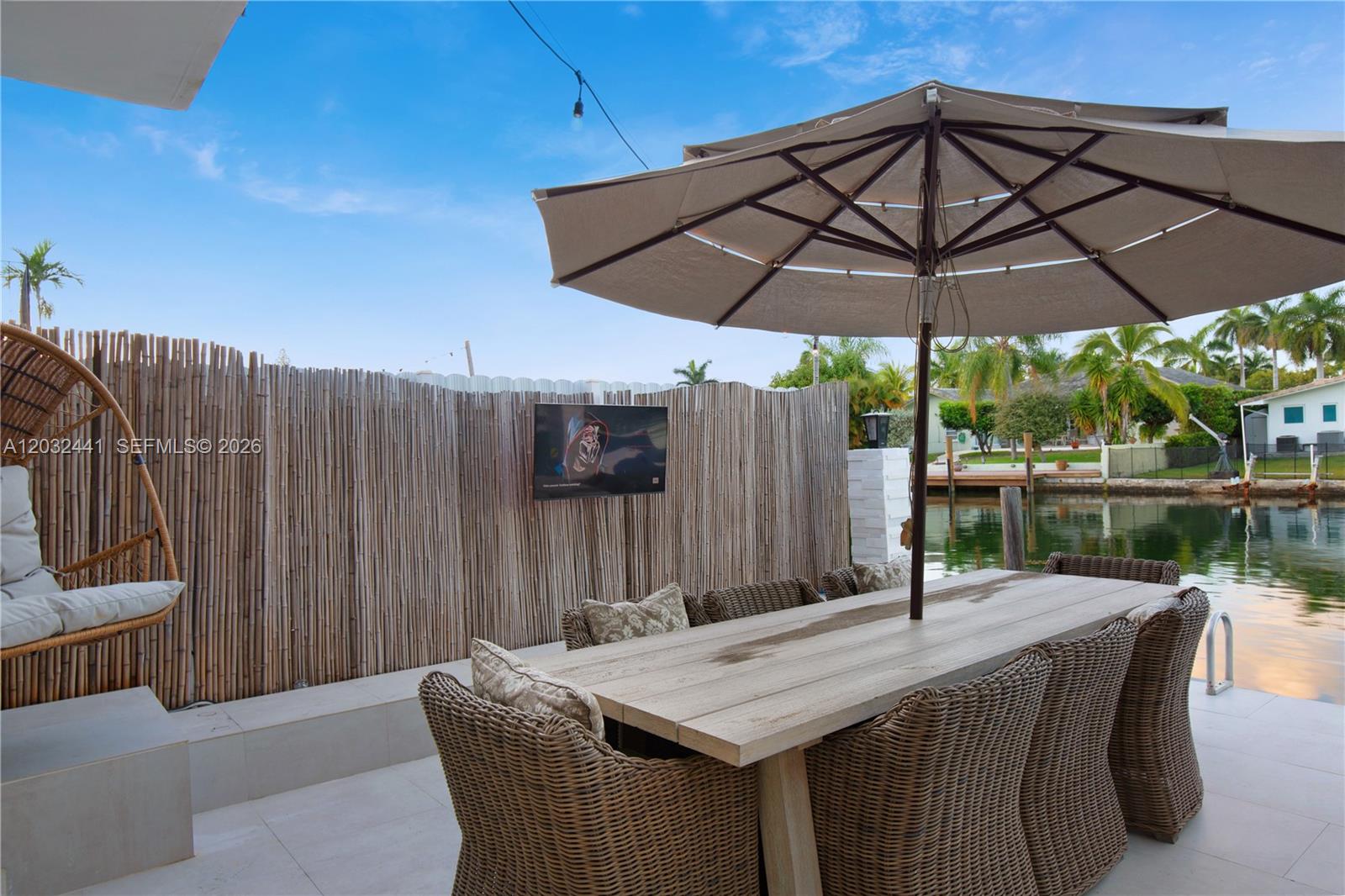 A patio with a dining table, umbrella, and television mounted on a bamboo privacy fence — 2115 NE 123rd St, North Miami FL 33181, NORTH MIAMI, FL