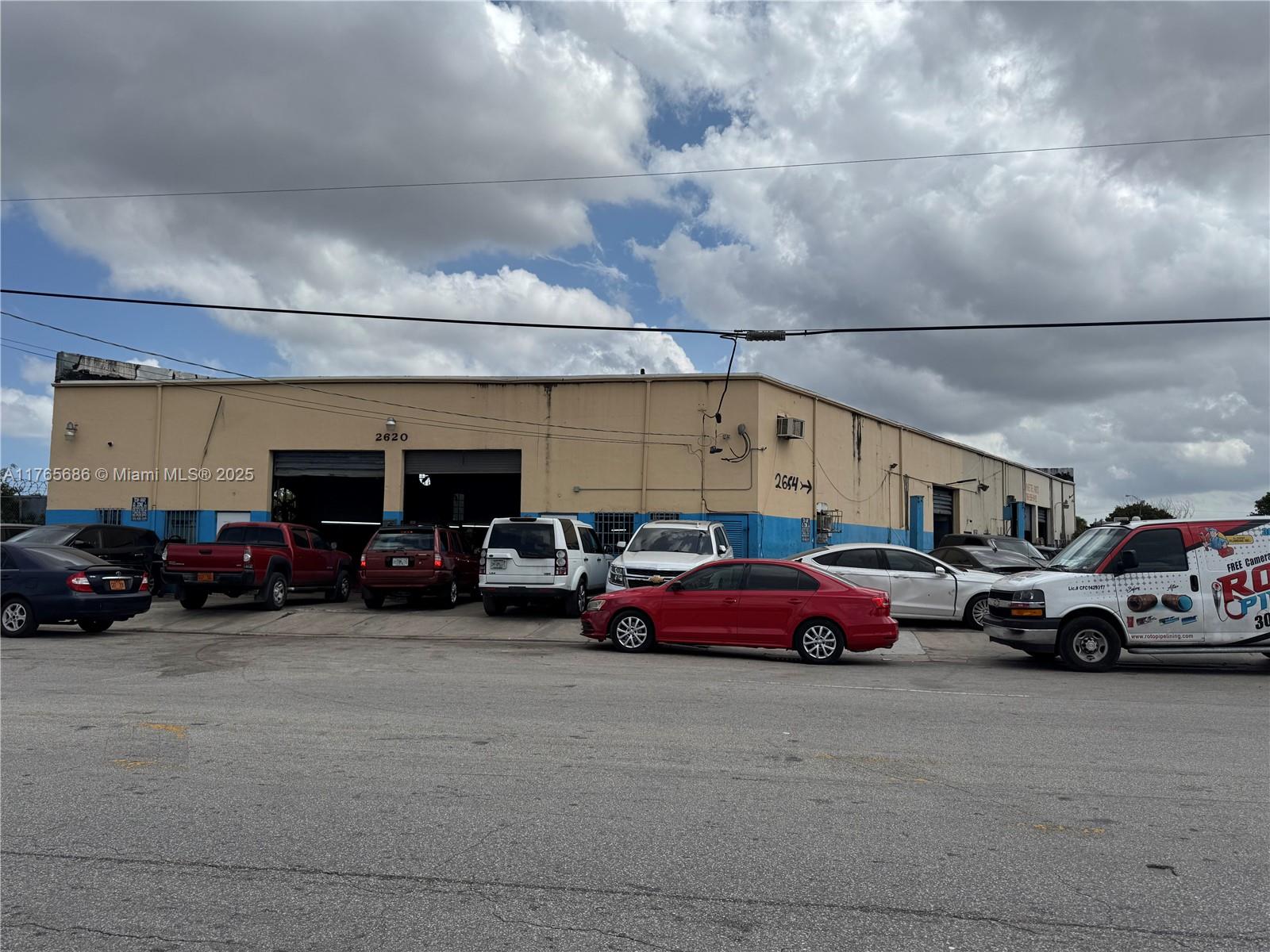 An exterior view of a commercial warehouse building with multiple garage bays and parked vehicles — 2620 SW Ali Baba Ave, Opa-Locka FL 33054, OPA-LOCKA, FL