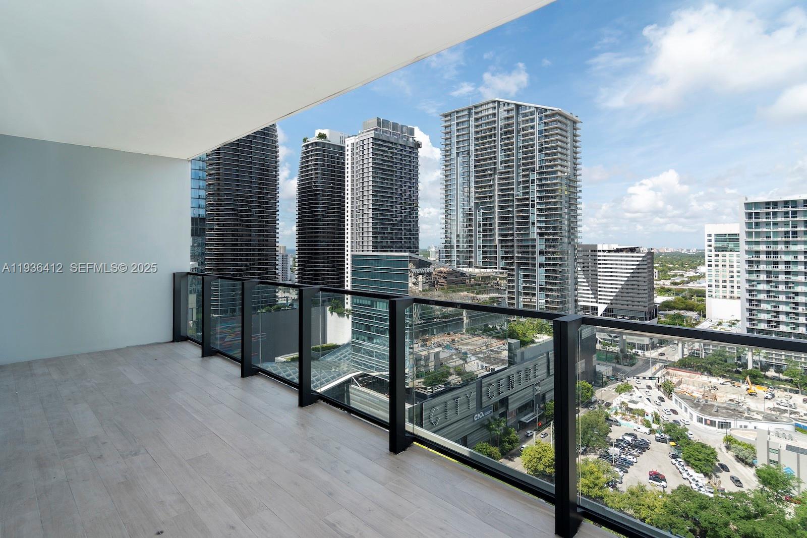 A high-rise balcony with light wood-look flooring and a glass railing overlooks a city skyline — 68 SE 6th St # 2010, Miami FL 33131, MIAMI, FL