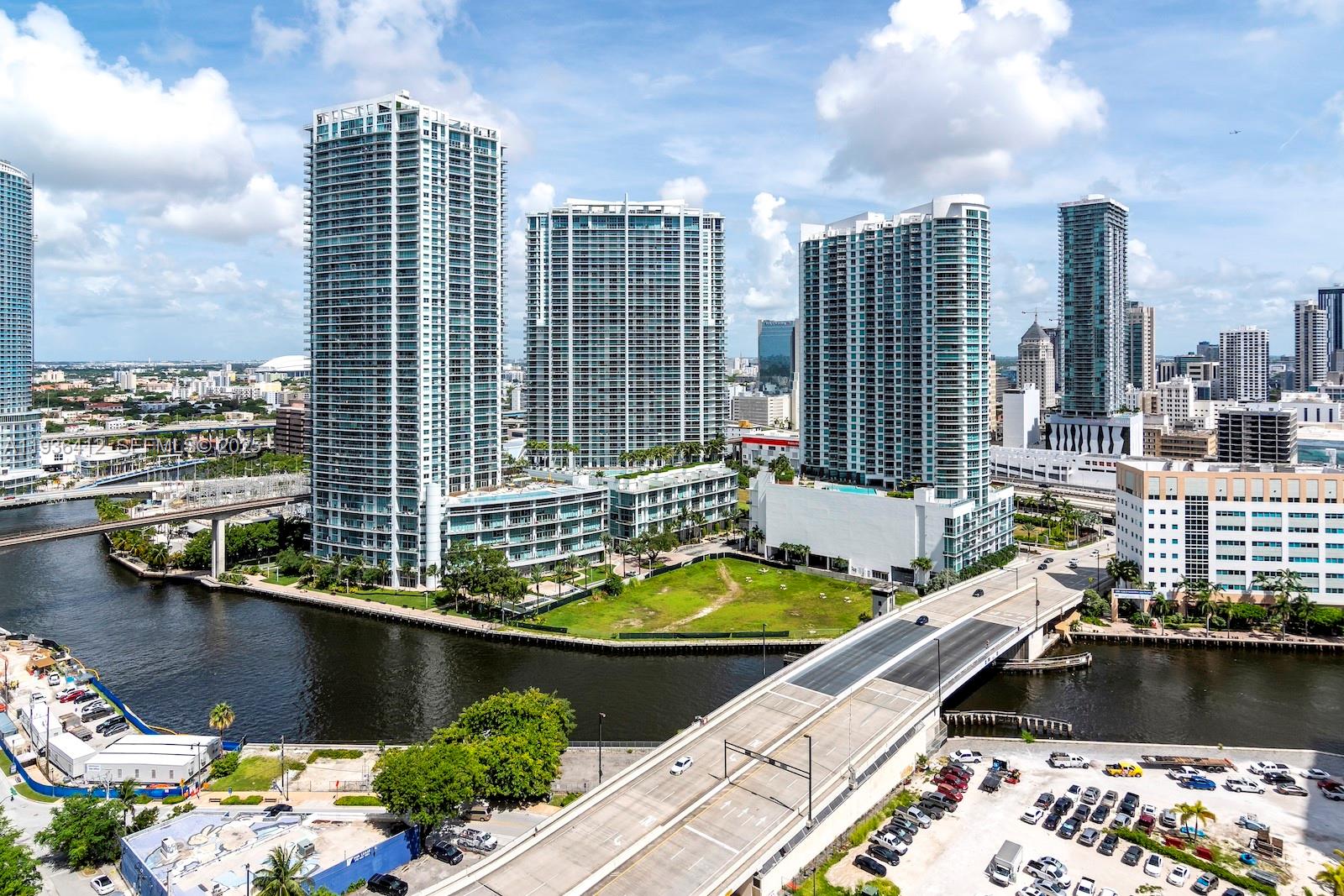 An aerial view shows high-rise apartment buildings near a river, a bridge, and parking lots — 68 SE 6th St # 2010, Miami FL 33131, MIAMI, FL