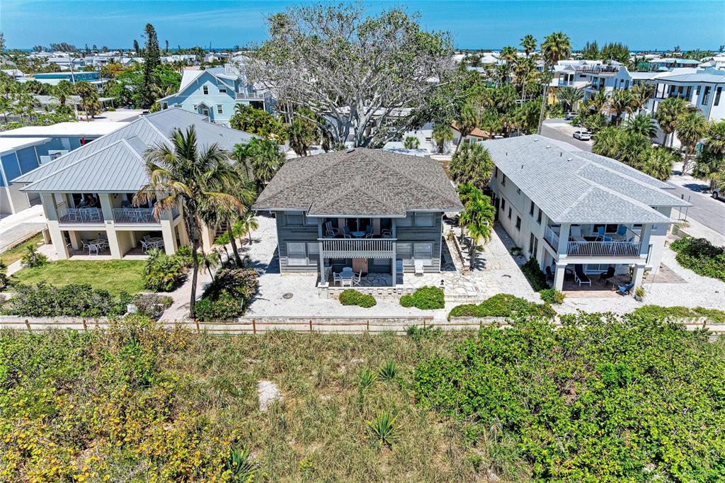 An aerial view shows three multi-story houses with metal roofs situated near a sandy beach — 102 PALMETTO AVENUE, ANNA MARIA, FL