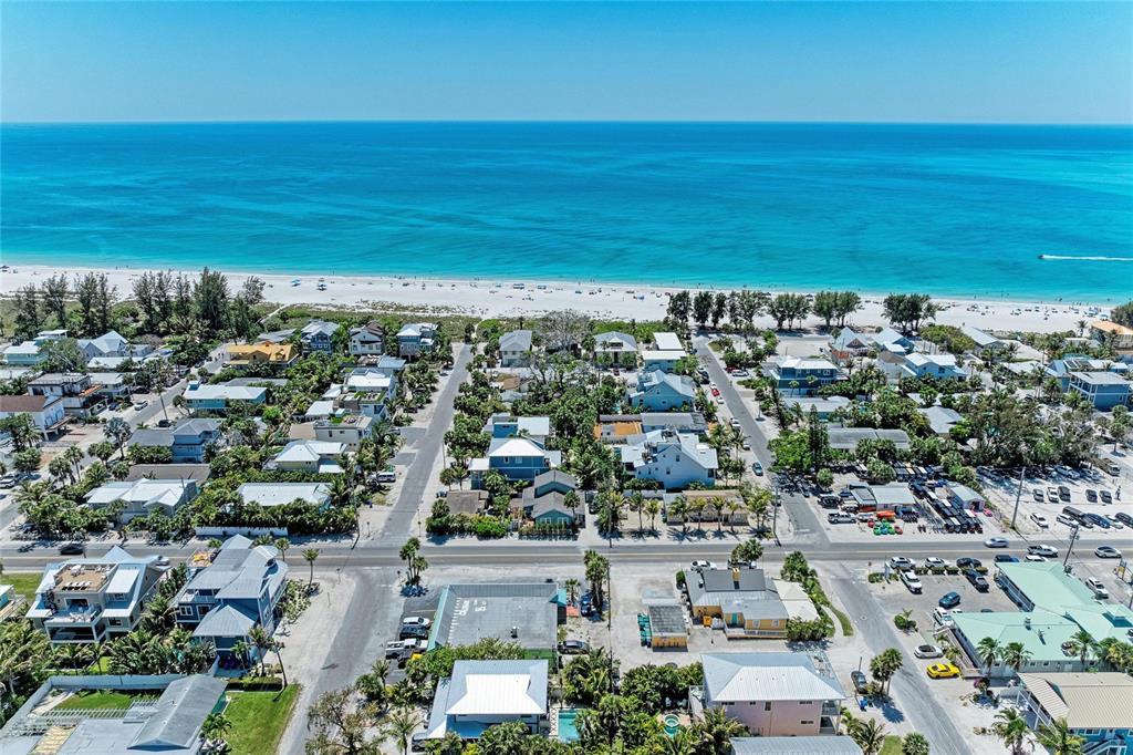An aerial view shows a coastal neighborhood with houses, streets, and a sandy beach — 102 PALMETTO AVENUE, ANNA MARIA, FL