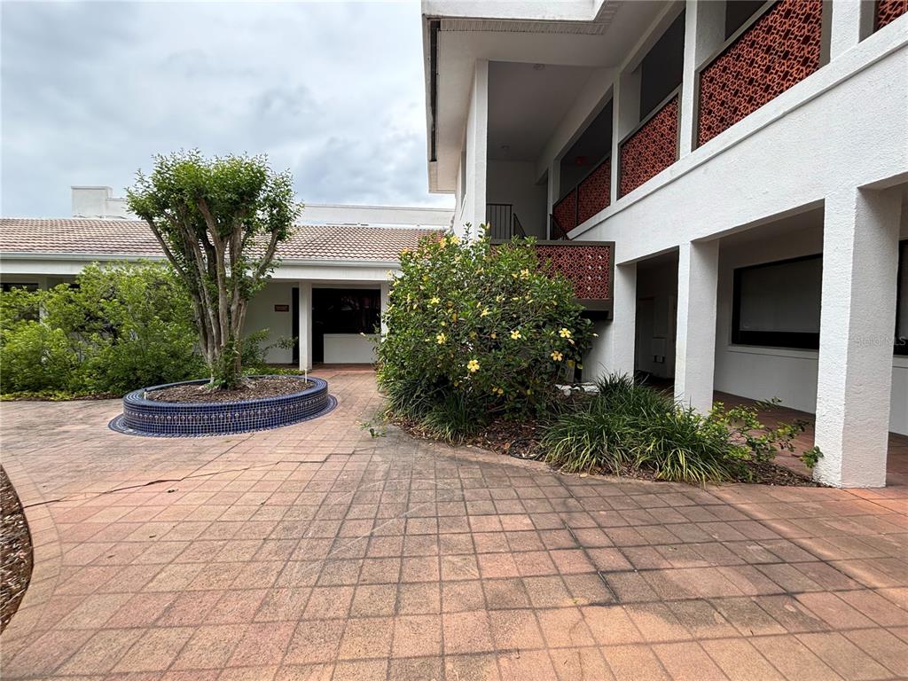 A paved courtyard features a circular tiled planter and a two-story building with decorative screens — 1750 W BROADWAY STREET UNIT 112, OVIEDO, FL