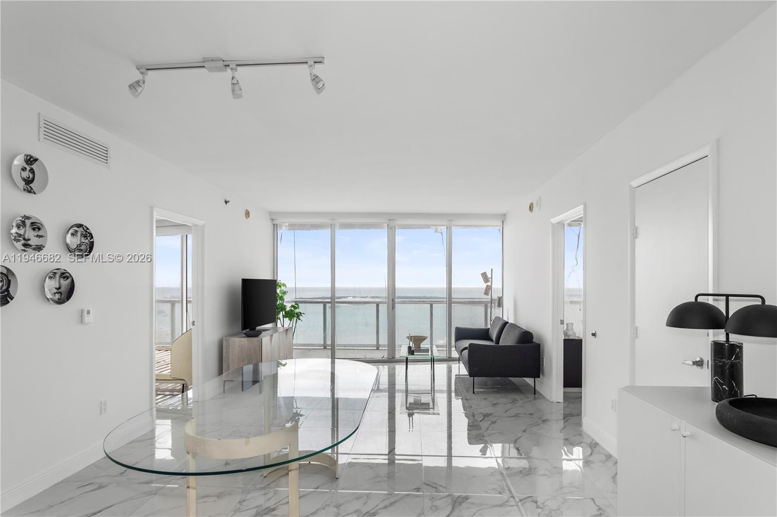 A bright living and dining area features white marble floors, a glass table, and ocean views — 465 Brickell Ave # 5505, Miami FL 33131, MIAMI, FL