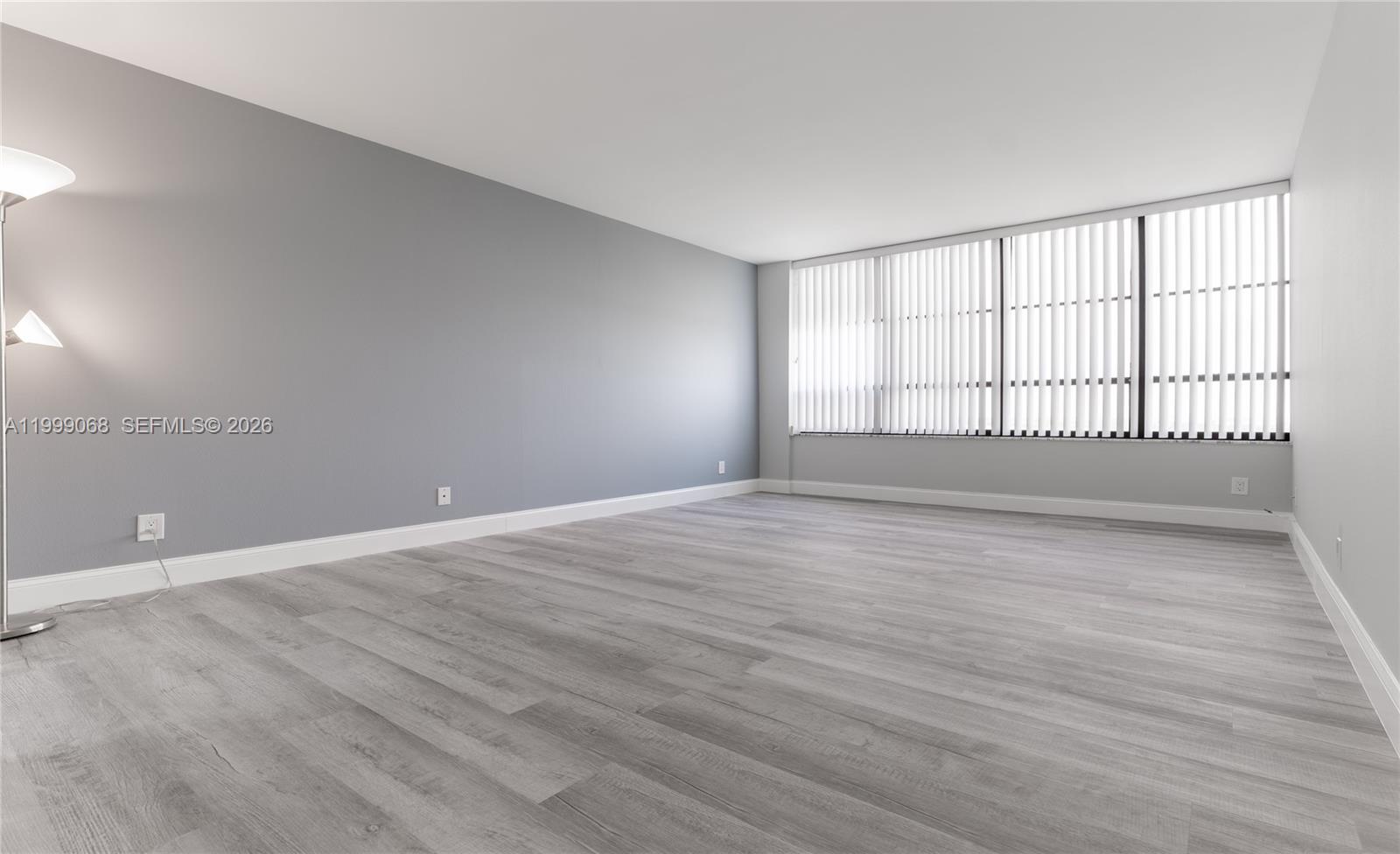 An empty room features gray walls, light wood-look flooring, and large windows with vertical blinds — 500 Three Islands Blvd # 1110, Hallandale Beach FL 33009, HALLANDALE BEACH, FL