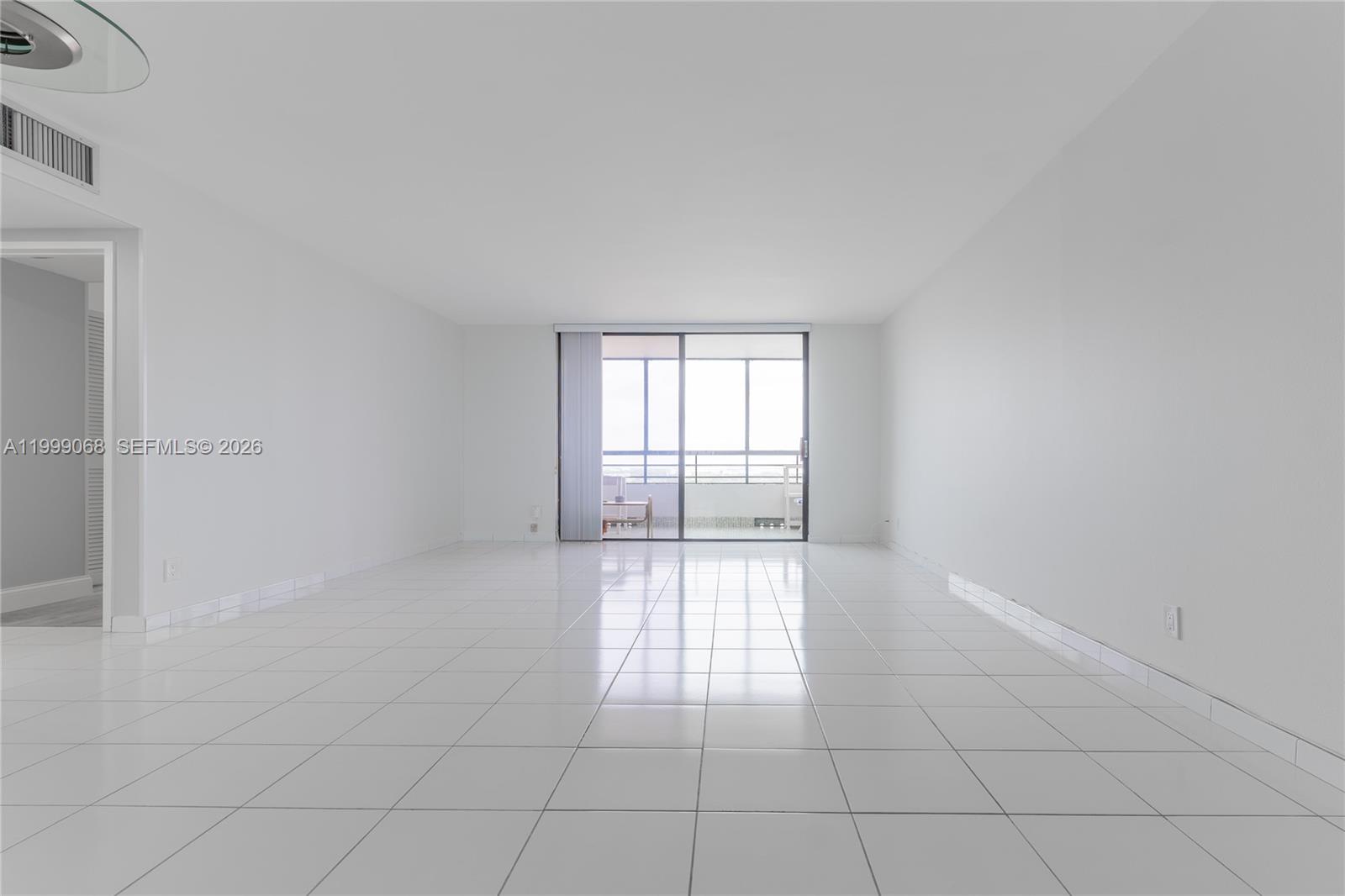 An empty room features white tile flooring, plain white walls, and a sliding glass balcony door — 500 Three Islands Blvd # 1110, Hallandale Beach FL 33009, HALLANDALE BEACH, FL