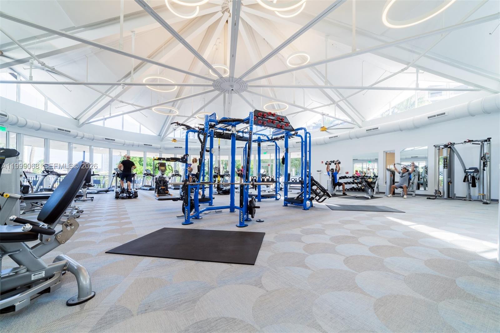 A bright, circular gym features a high vaulted ceiling, blue fitness equipment, and patterned flooring — 500 Three Islands Blvd # 1110, Hallandale Beach FL 33009, HALLANDALE BEACH, FL