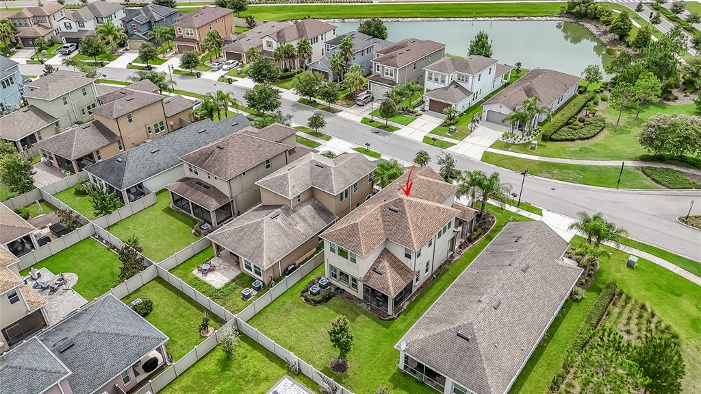 An aerial view shows a suburban neighborhood with houses, fenced backyards, and a small lake — 4459 TRAMANTO LANE, WESLEY CHAPEL, FL