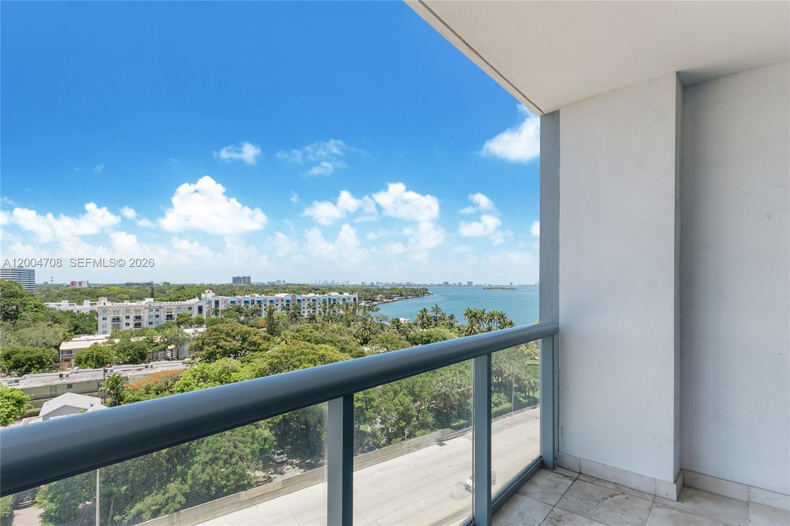 A balcony with a glass railing overlooks a coastal landscape with trees and water — 601 NE 36th St # 801, Miami FL 33137, MIAMI, FL