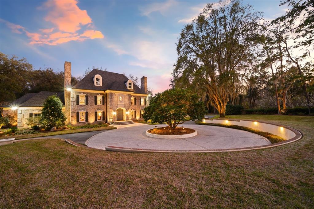 A two-story brick house features a circular driveway with a central tree at dusk — 623 SW 93RD STREET, GAINESVILLE, FL
