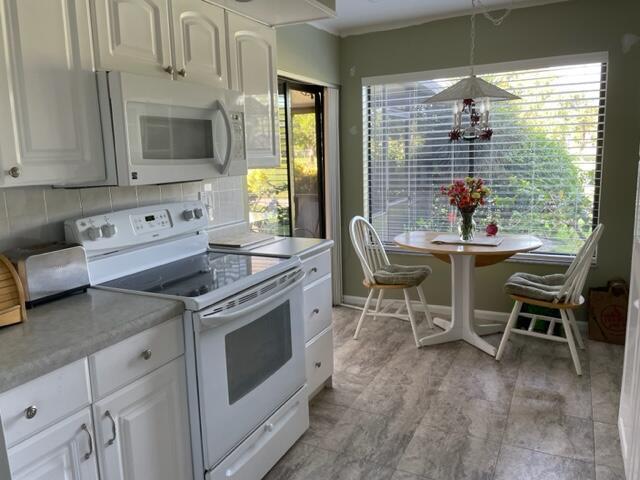 A kitchen features white cabinetry, a white stove, and a small dining table by windows — 36 Ironwood Way N # 36, Palm Beach Gardens FL 33418, PALM BEACH GARDENS, FL