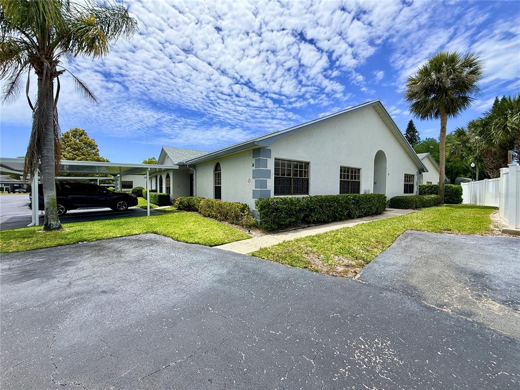 A single-story house with a carport, palm trees, and a paved driveway under a cloudy sky — 2749 COUNTRYSIDE BOULEVARD UNIT 14, CLEARWATER, FL