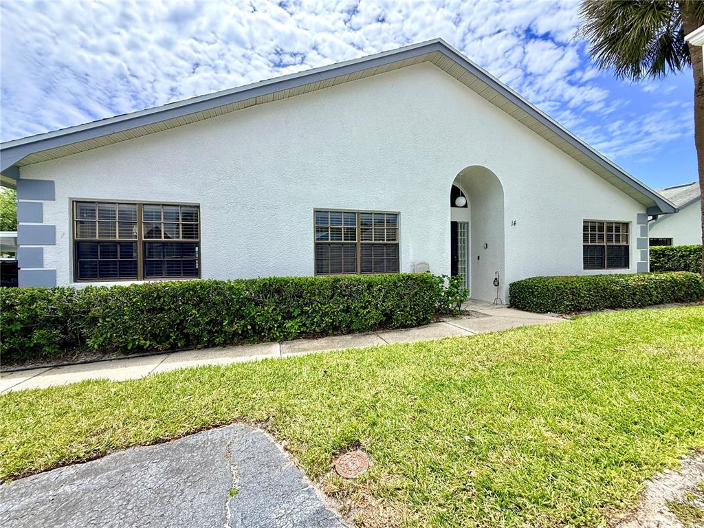 A white single-story house features a front entrance, windows with shutters, and manicured hedges — 2749 COUNTRYSIDE BOULEVARD UNIT 14, CLEARWATER, FL