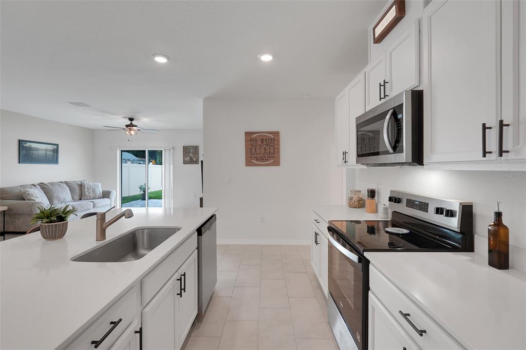 A modern kitchen with white cabinets and quartz countertops overlooks a living room and patio — 3615 SALVIA COURT, TAVARES, FL