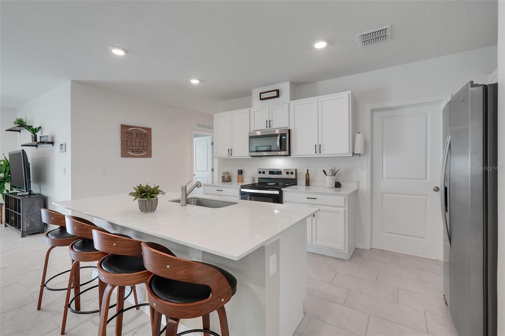 A modern kitchen features white cabinets, stainless steel appliances, and a large central island — 3615 SALVIA COURT, TAVARES, FL
