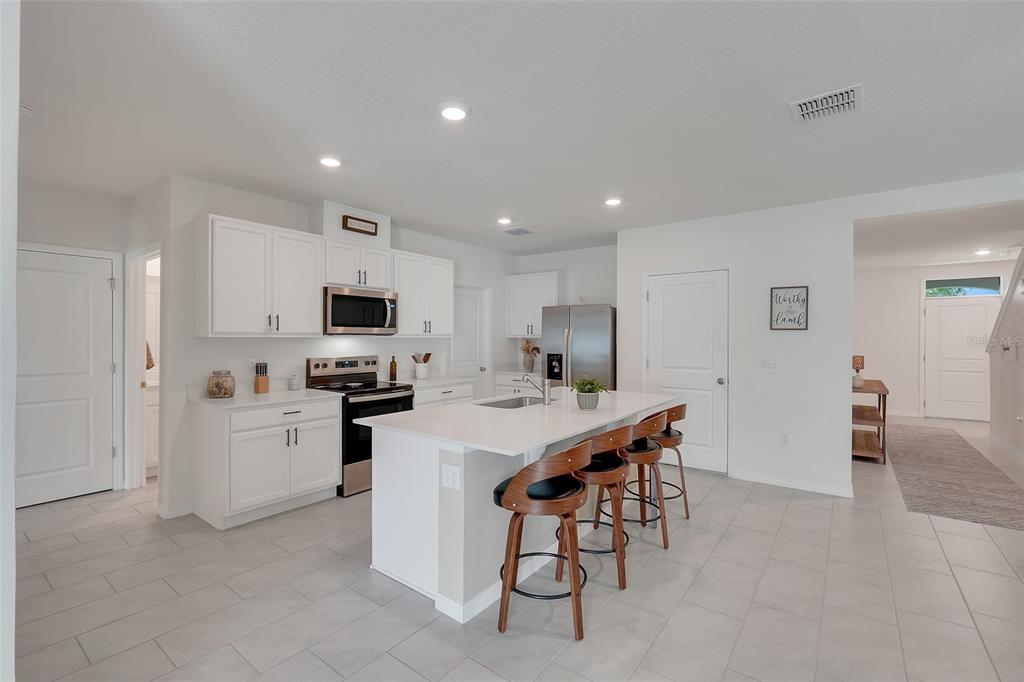 A modern kitchen features white cabinetry, a central island with bar stools, and tile flooring — 3615 SALVIA COURT, TAVARES, FL