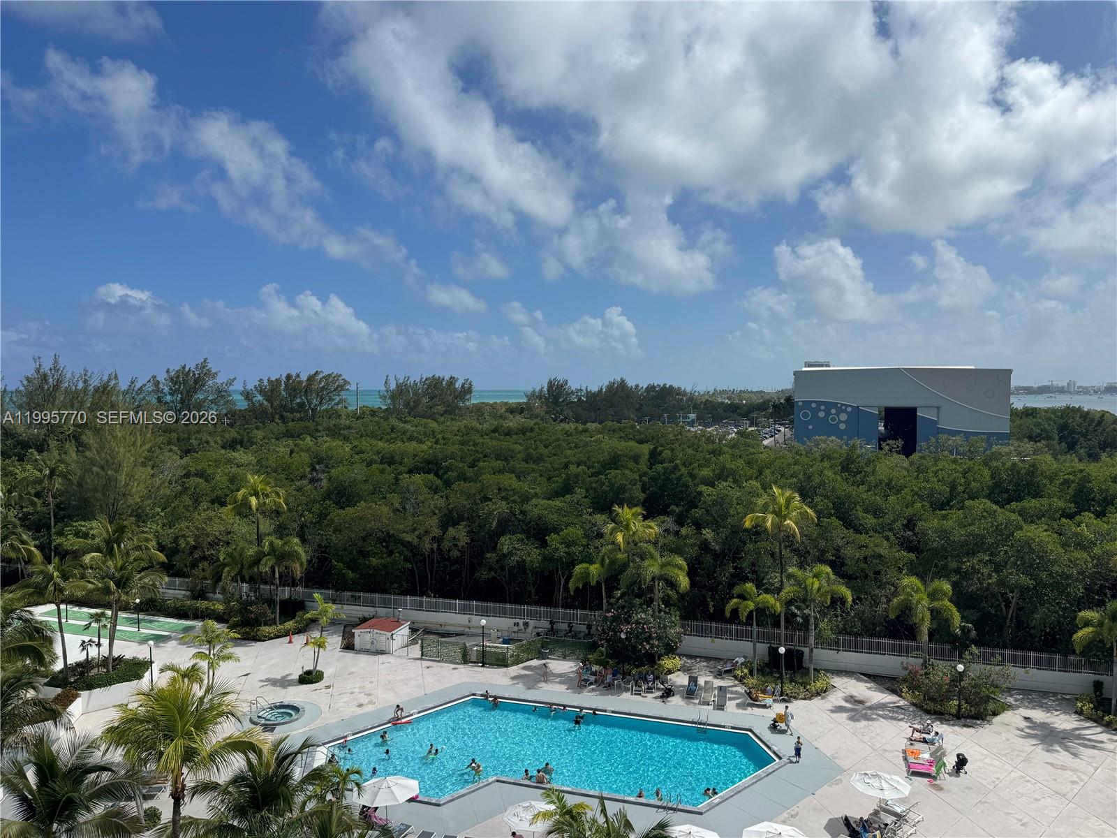 An elevated view shows a swimming pool surrounded by palm trees and dense green vegetation — 100 Bayview Dr # 725, Sunny Isles Beach FL 33160, SUNNY ISLES BEACH, FL