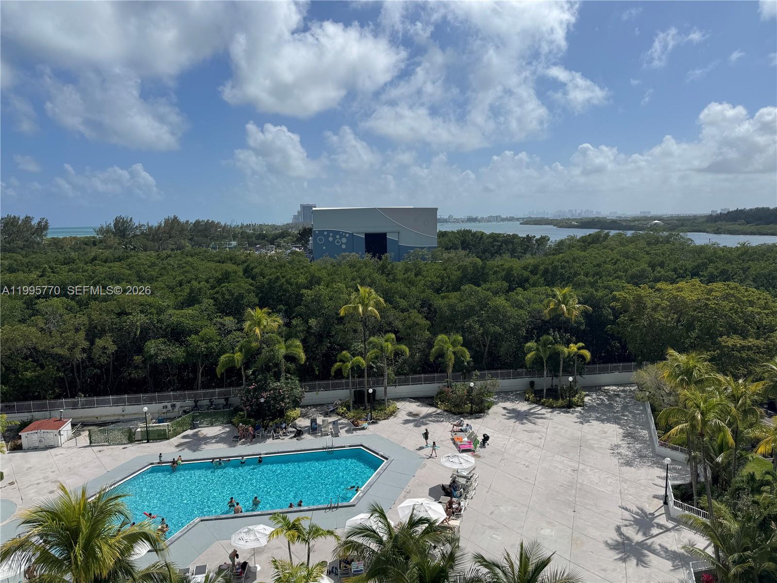 An elevated view shows a swimming pool surrounded by a patio and lush trees — 100 Bayview Dr # 725, Sunny Isles Beach FL 33160, SUNNY ISLES BEACH, FL