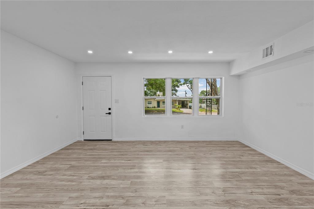 A bright, empty living room features white walls, recessed lighting, and light wood-look flooring — 1435 EDEN DRIVE, APOPKA, FL