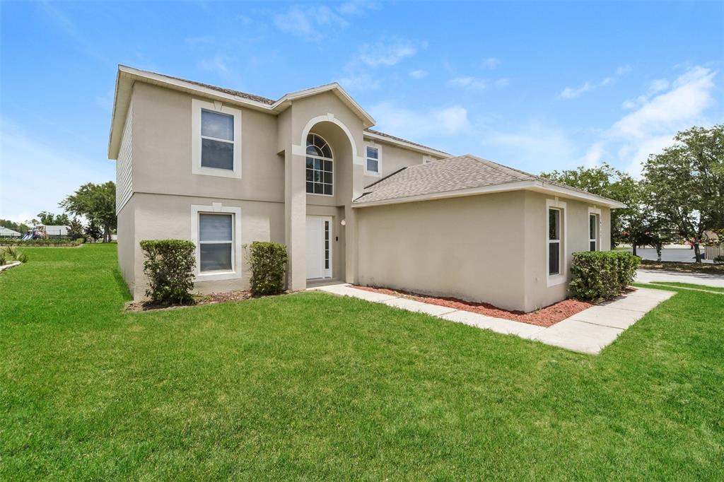 A two-story beige house with a front entrance, arched window, and a grassy lawn — 16249 WILKINSON DRIVE, CLERMONT, FL