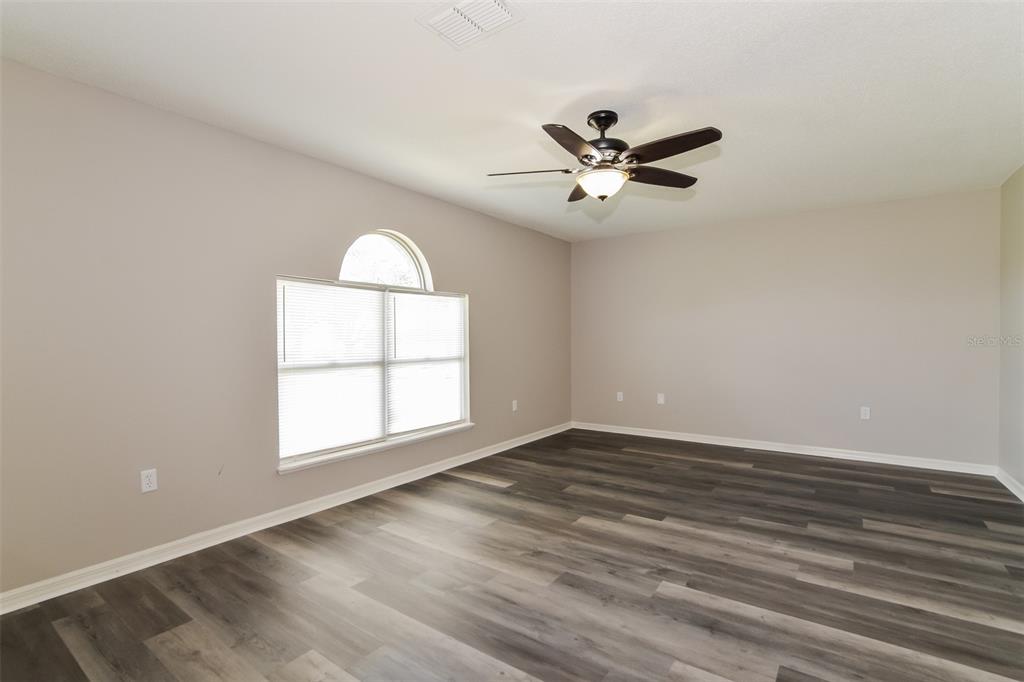 An empty room with light gray walls, dark wood-look flooring, and an arched window — 16249 WILKINSON DRIVE, CLERMONT, FL