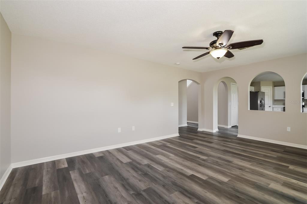An empty living room features gray wood-look flooring, beige walls, and arched wall openings — 16249 WILKINSON DRIVE, CLERMONT, FL
