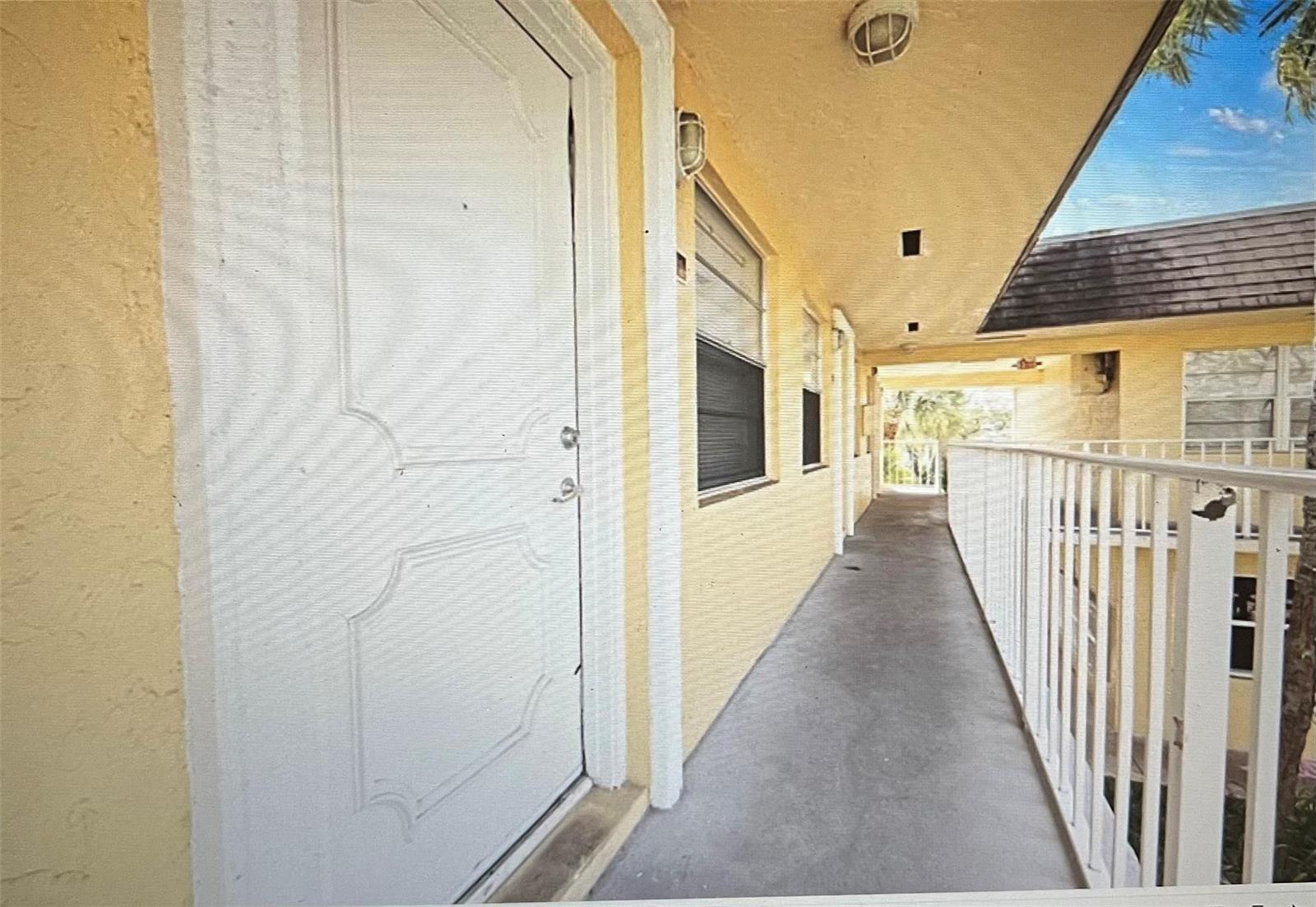 An exterior walkway with a white door, yellow stucco walls, and a white metal railing — 5150 NE 6th Avenue # 130, Oakland Park FL 33334, OAKLAND PARK, FL