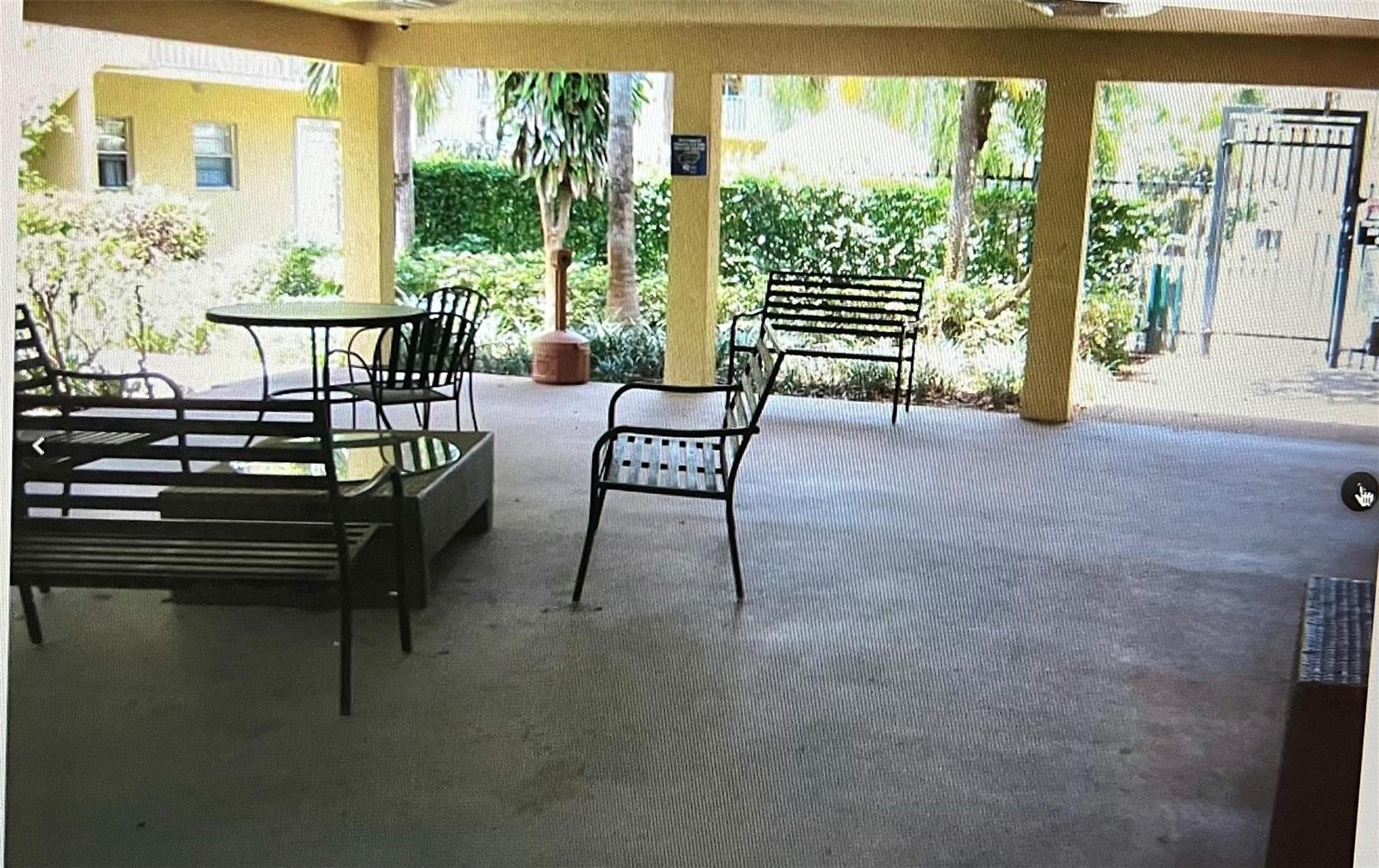 A covered outdoor patio features metal benches, a round table, and a view of landscaping — 5150 NE 6th Avenue # 130, Oakland Park FL 33334, OAKLAND PARK, FL