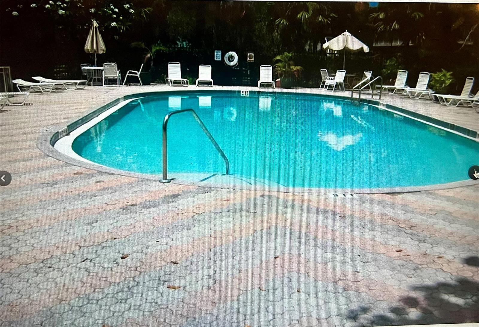 An outdoor swimming pool surrounded by a paved deck with lounge chairs and umbrellas — 5150 NE 6th Avenue # 130, Oakland Park FL 33334, OAKLAND PARK, FL